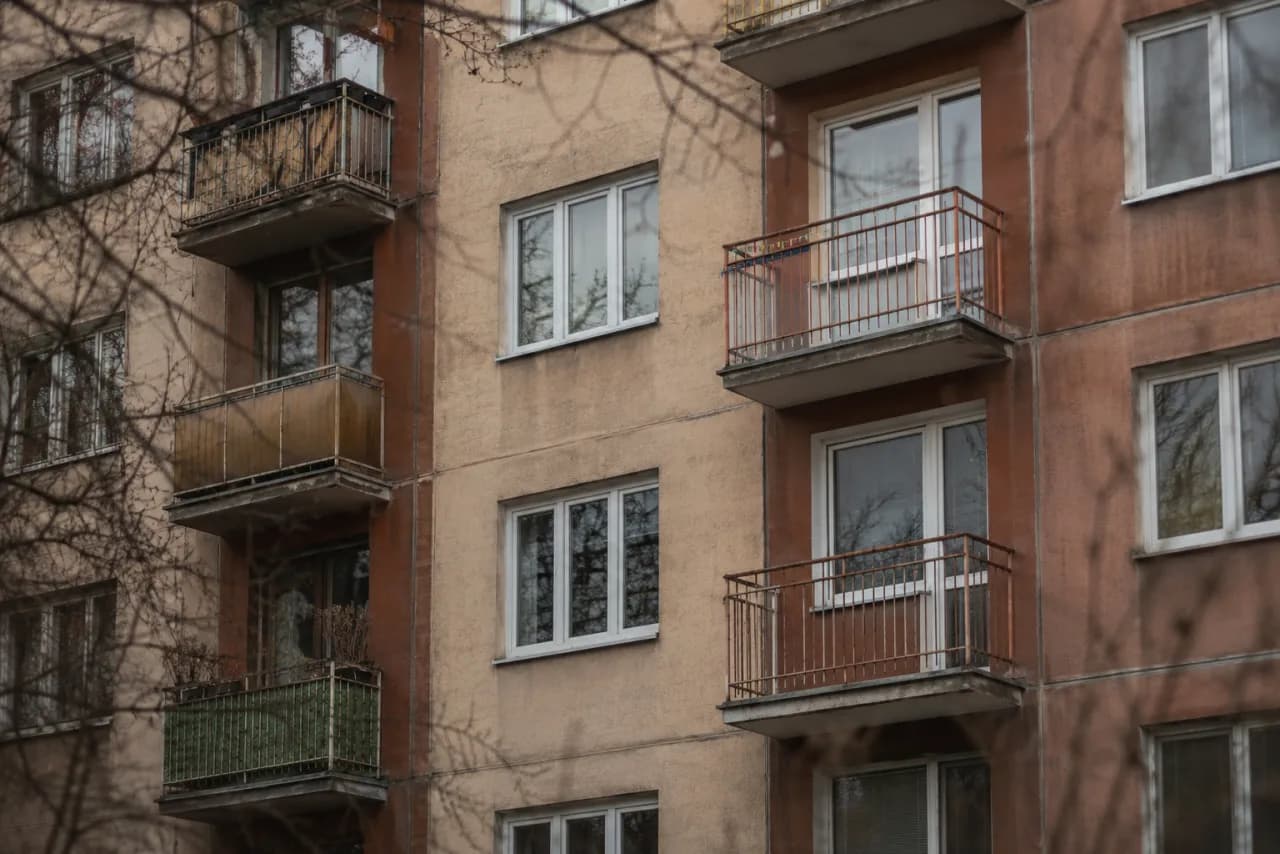 Starší panelový bytový dom s balkónmi a holými konármi stromov